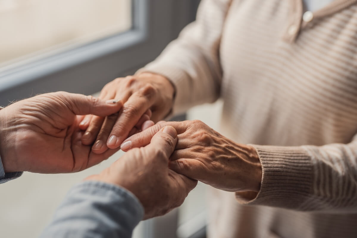 Elderly couple holding hands indoors by window