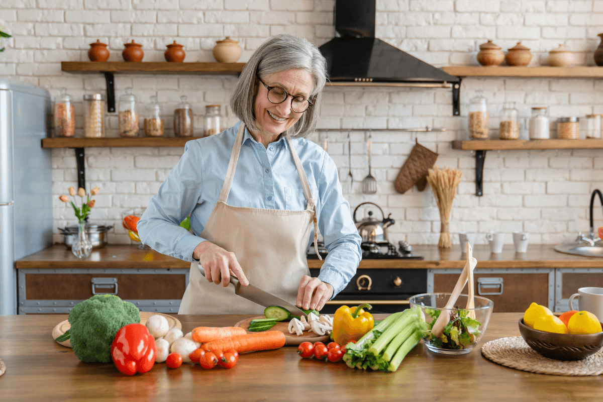 Mature woman slicing bell cucumber on wooden cutting board in modern home kitchen.