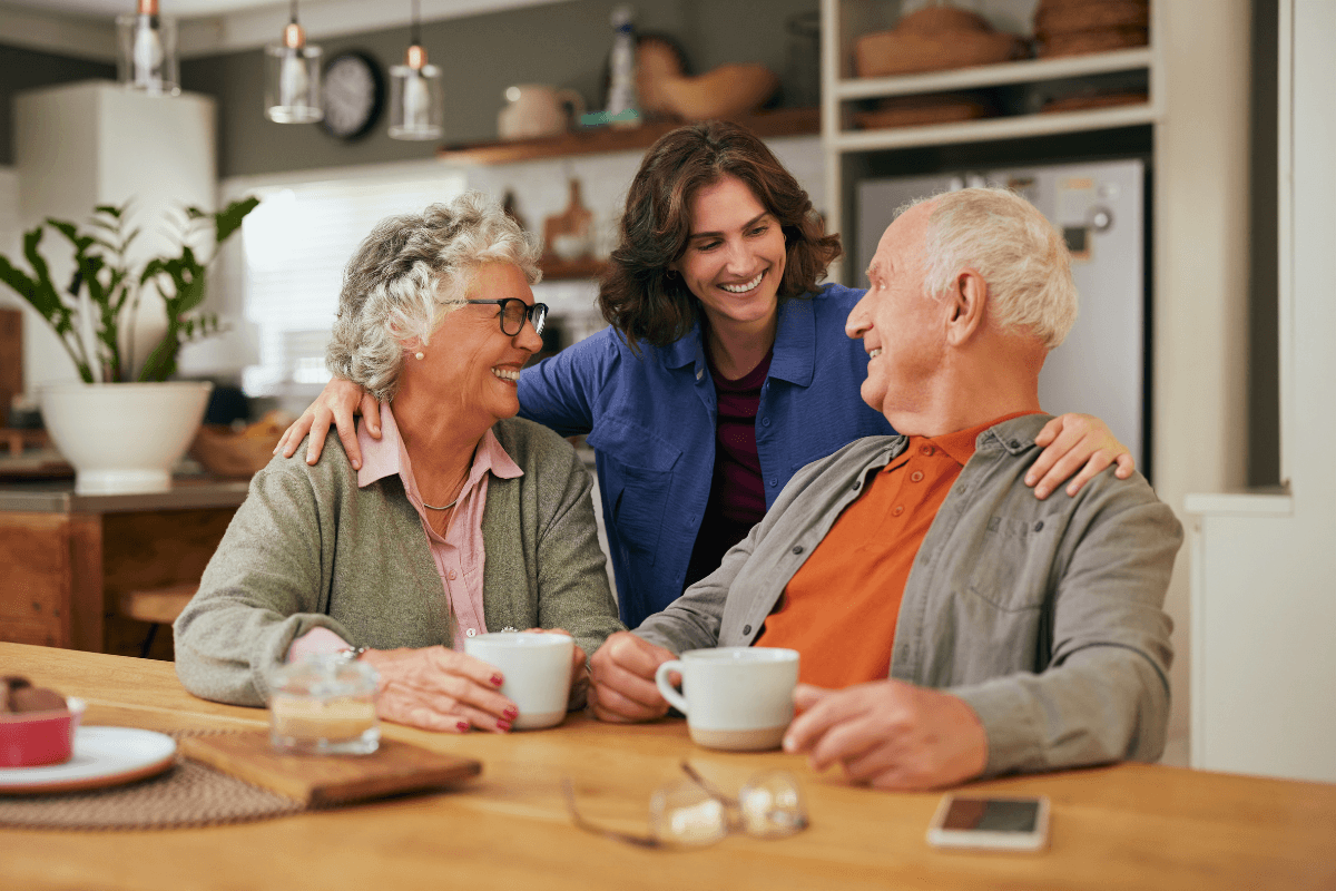 An elderly couple shares a warm cup of tea and heartfelt conversation with their daughter in the comfort of their home.