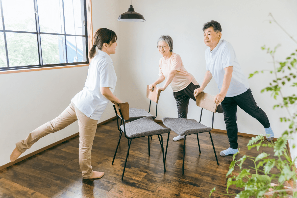Seniors stretching with chairs in bright room