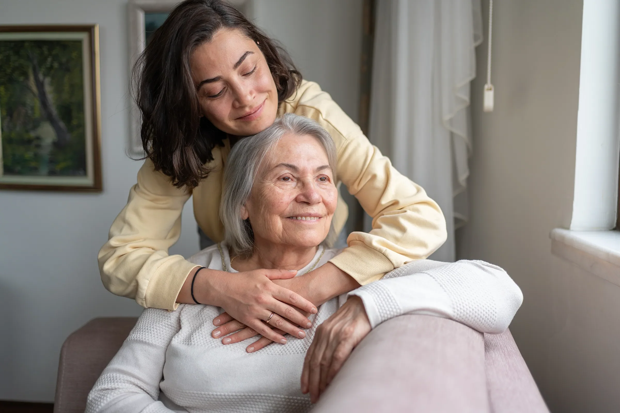 Young woman hugging elderly woman on couch