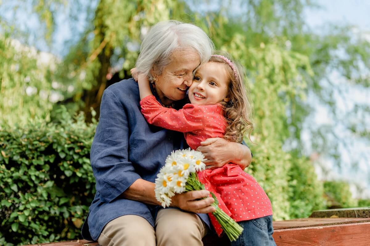 Grandmother and granddaughter hugging with daisies outdoors