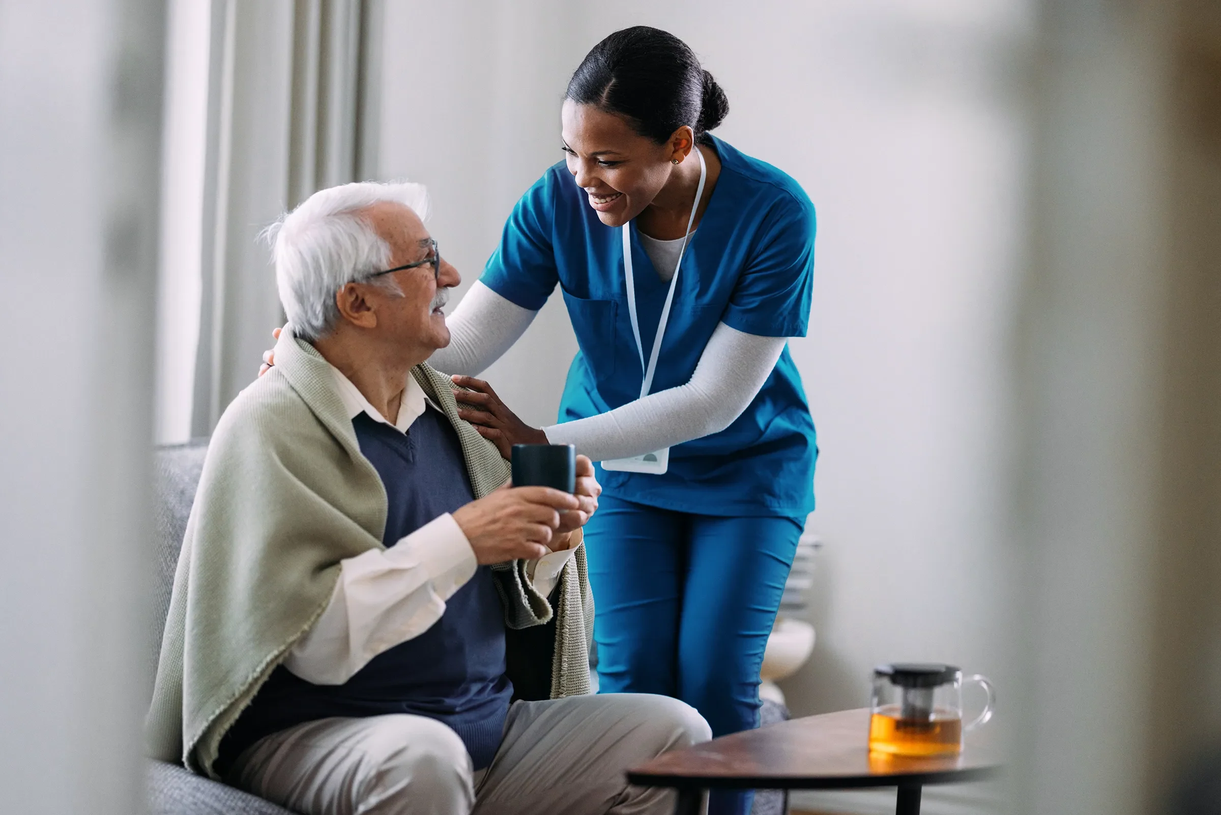 Caregiver assisting elderly man with warm drink
