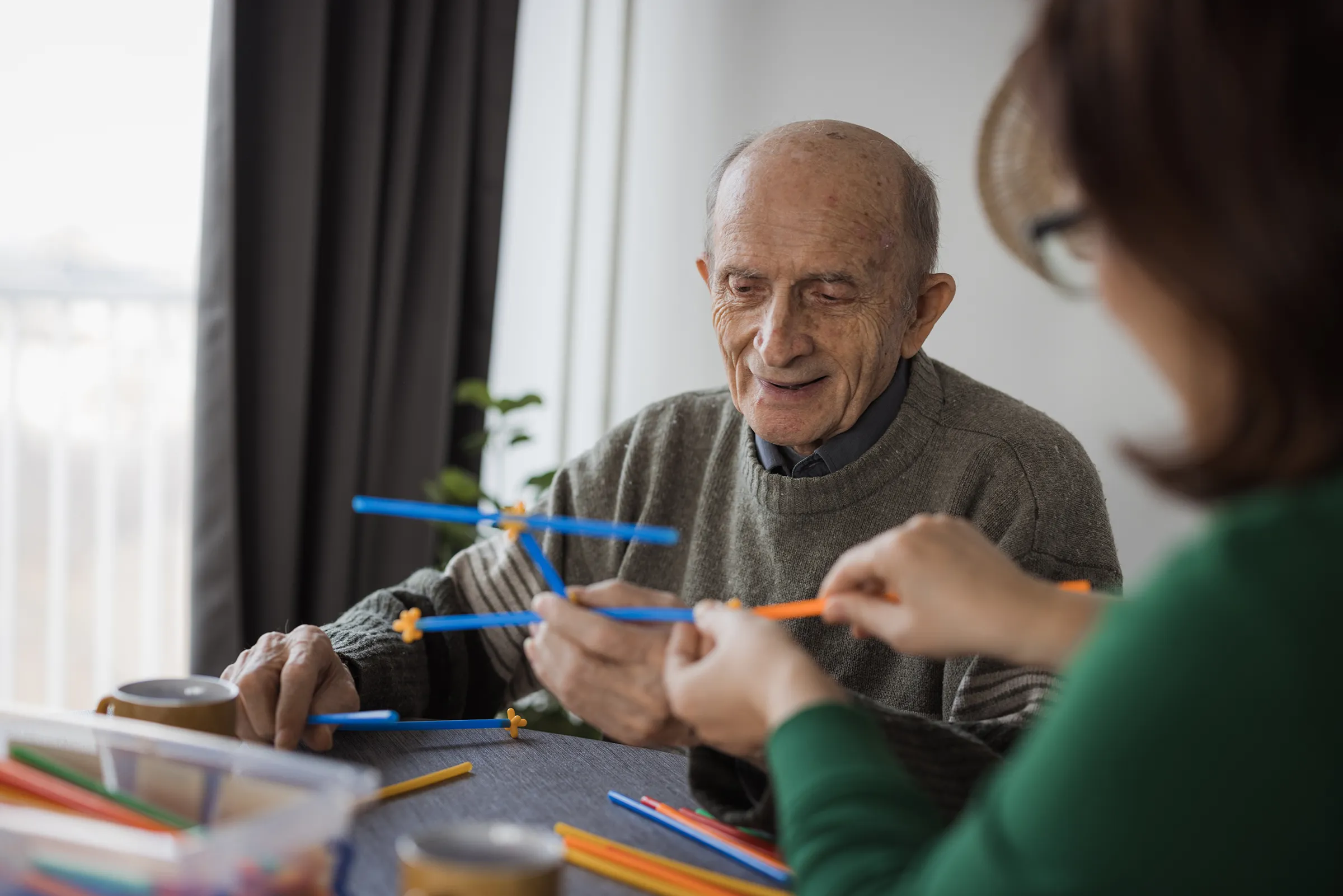 Elderly man assembling colorful plastic rods at table