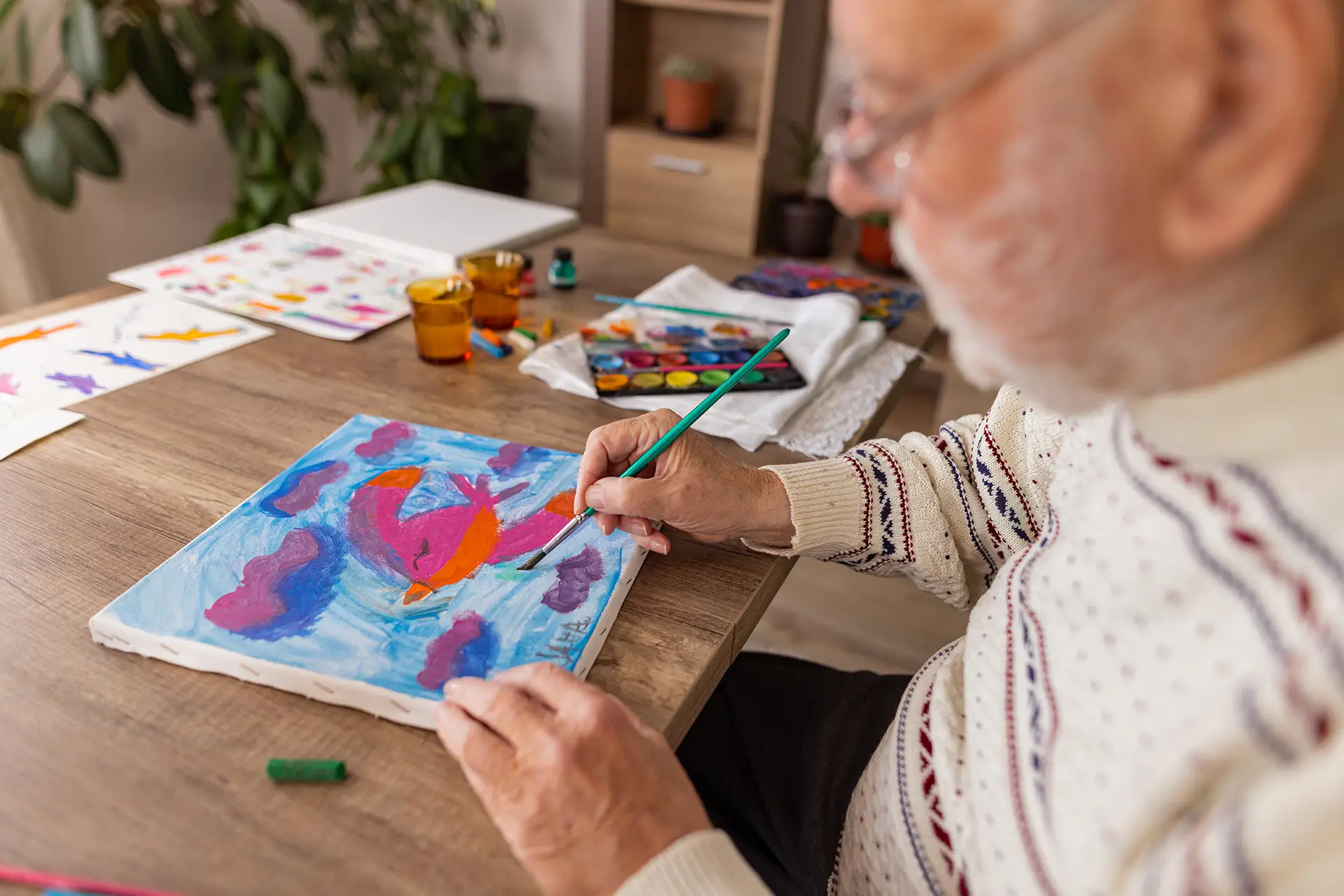 Elderly person painting colorful bird on canvas
