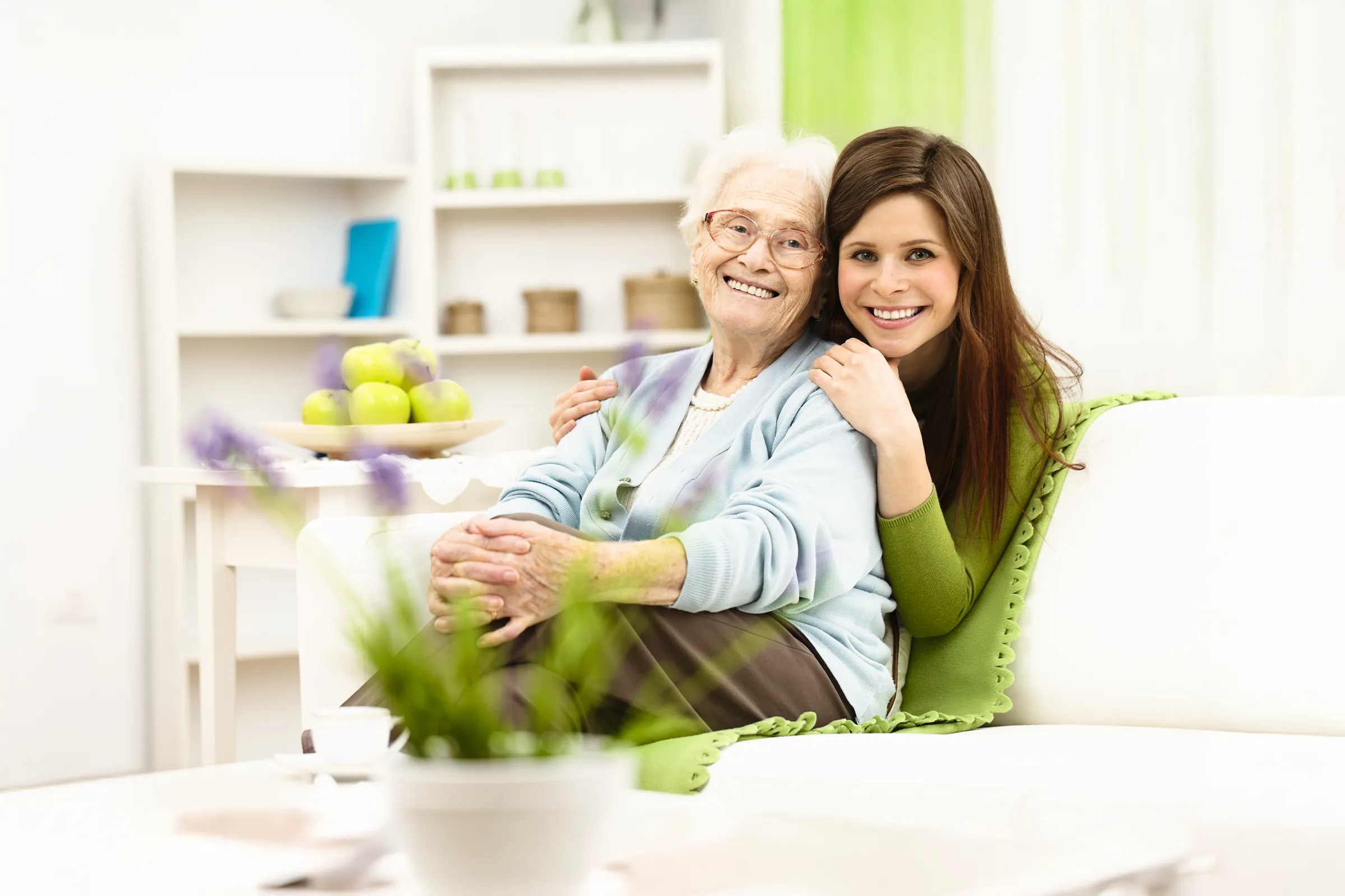 Young woman hugging smiling elderly woman on couch
