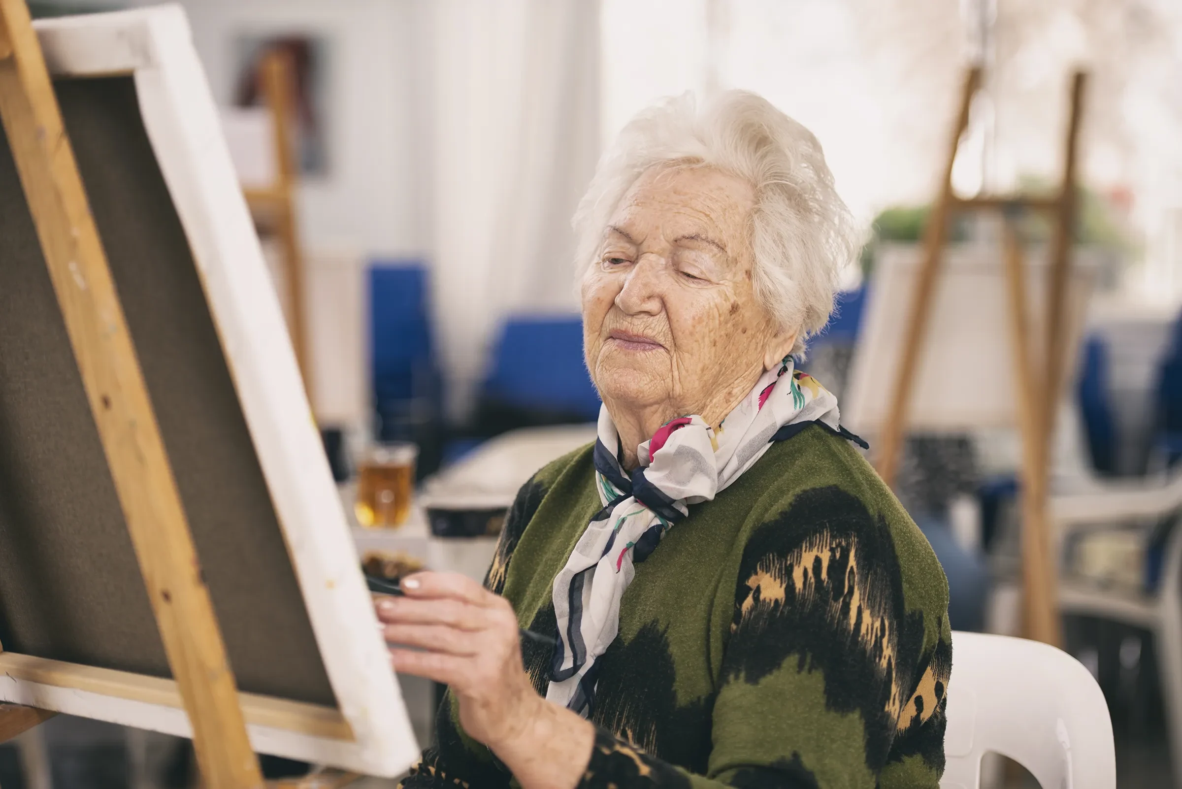 Elderly woman painting on canvas at easel