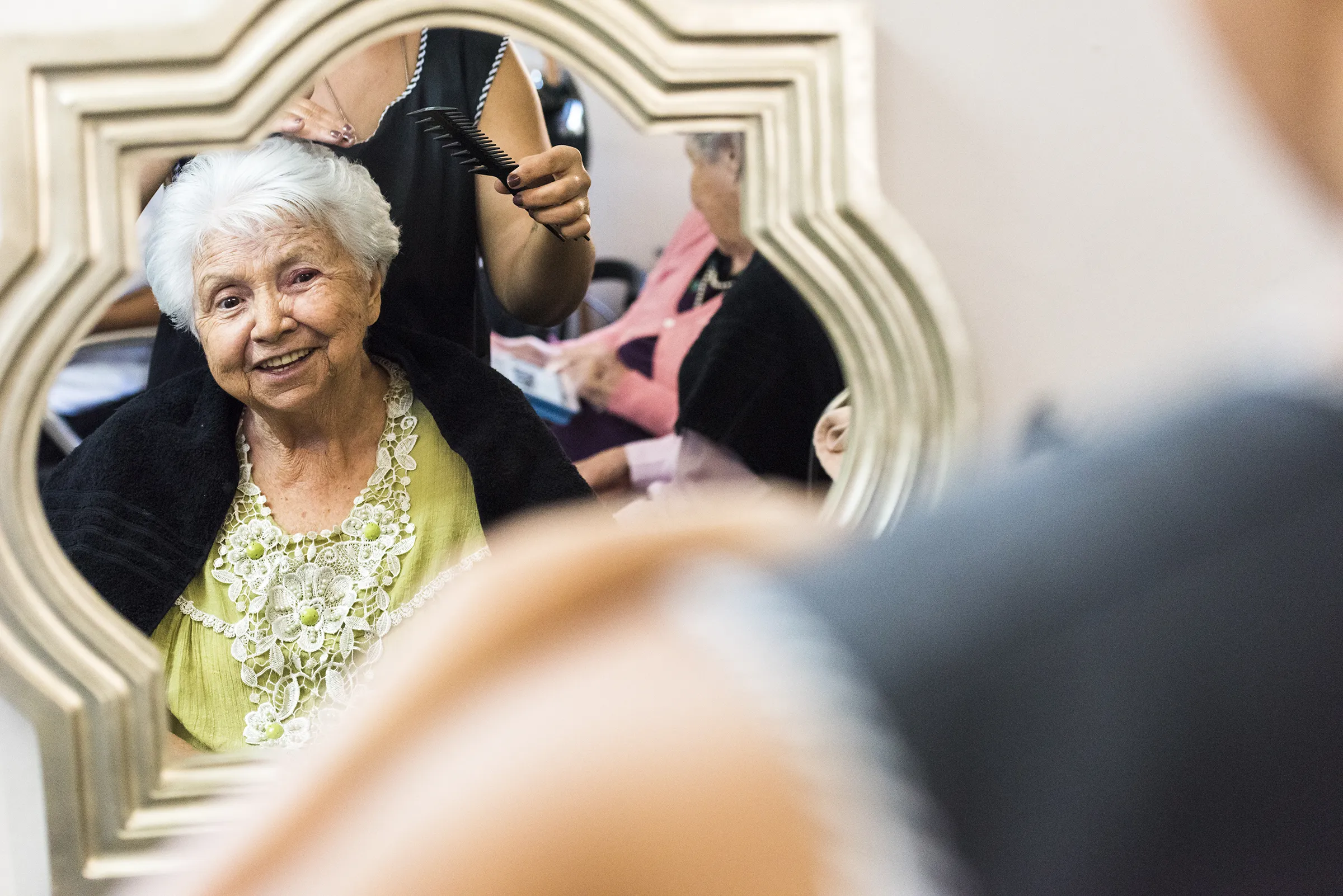 Elderly woman smiling at salon mirror during haircut