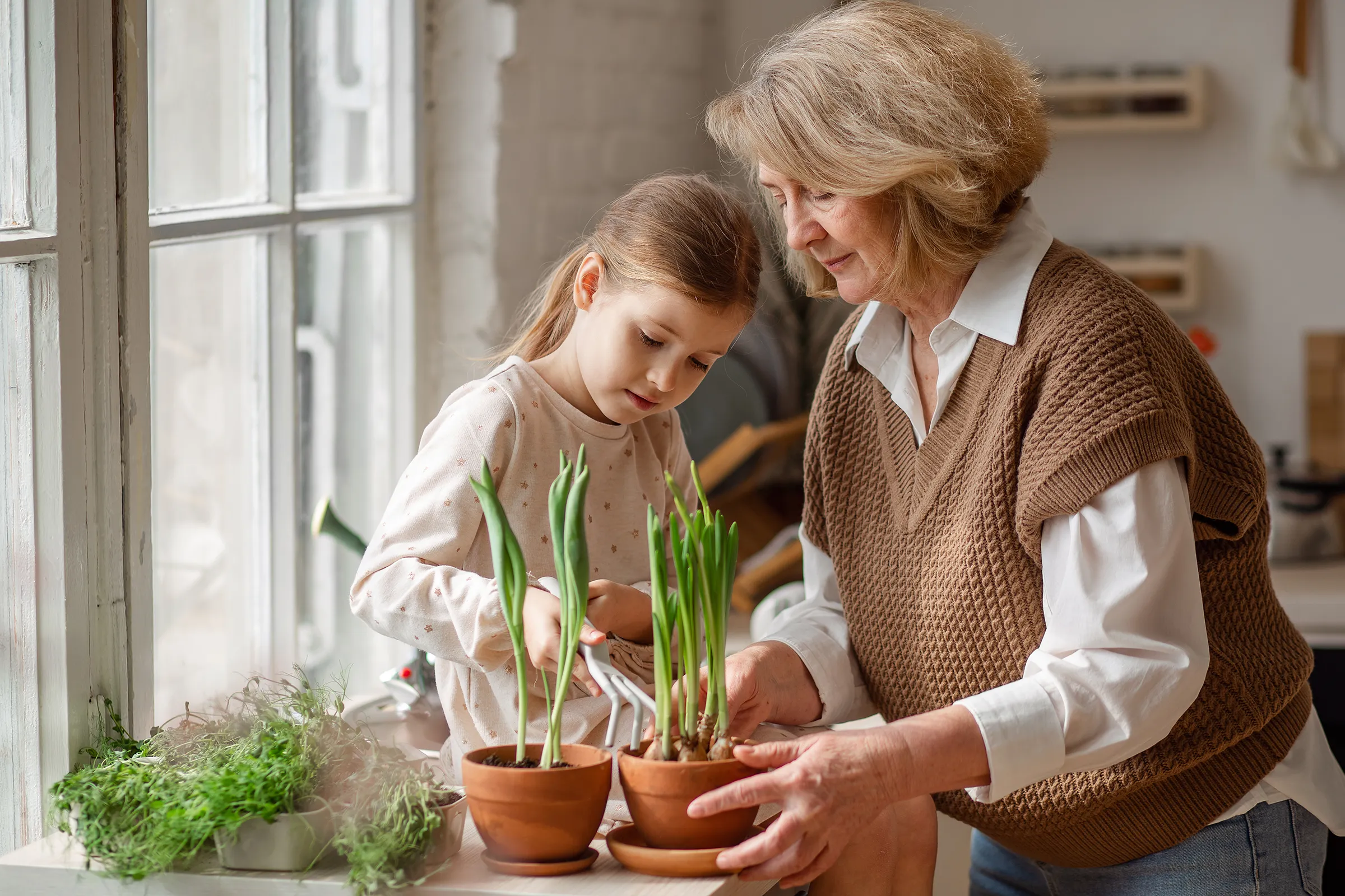 Grandmother and granddaughter watering potted plants indoors
