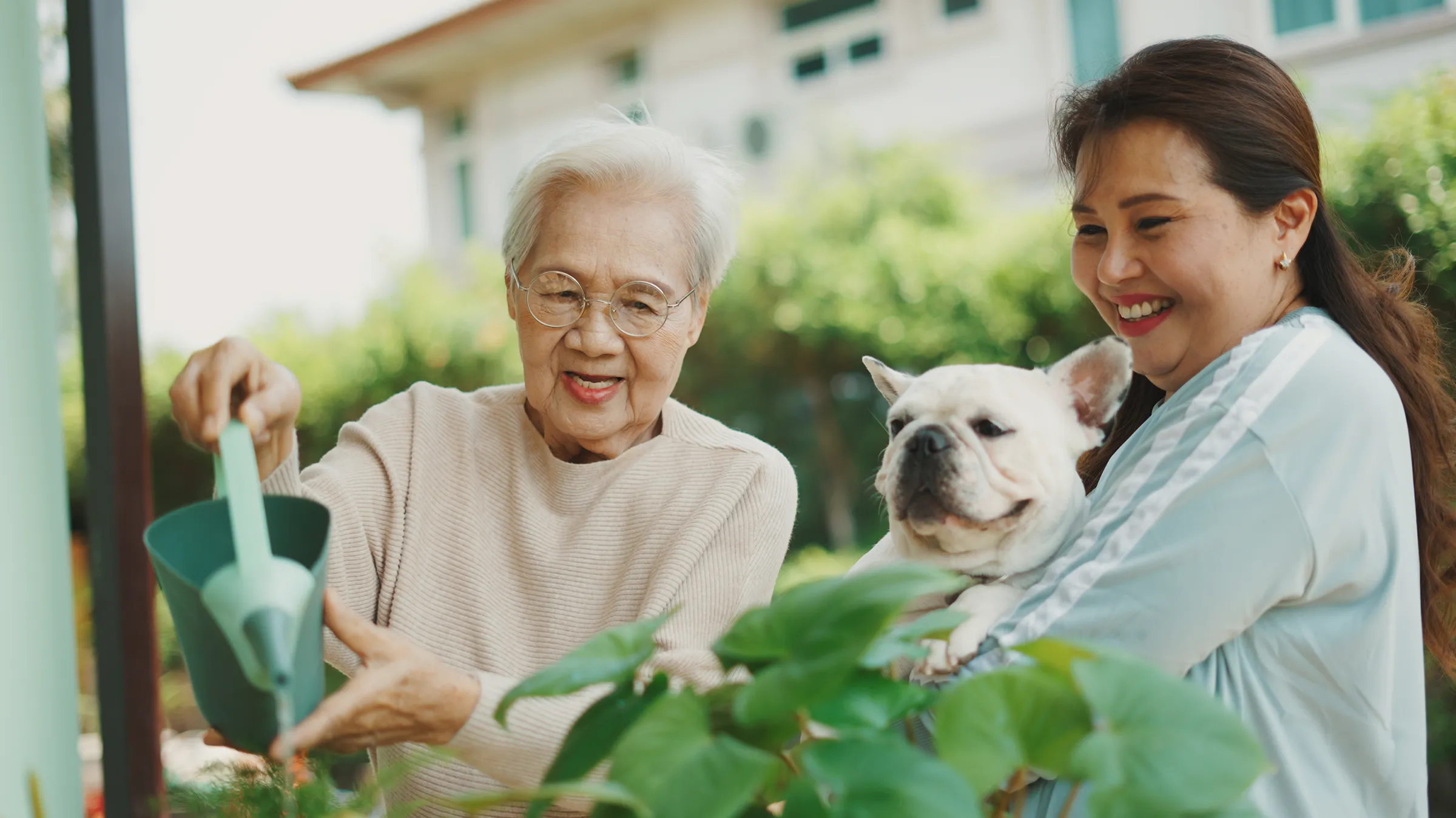 Grandmother watering plants beside woman holding dog