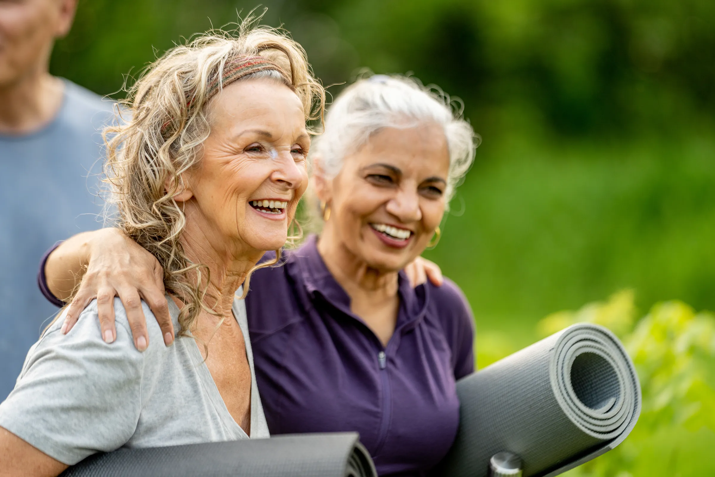 Two senior women holding yoga mats outdoors