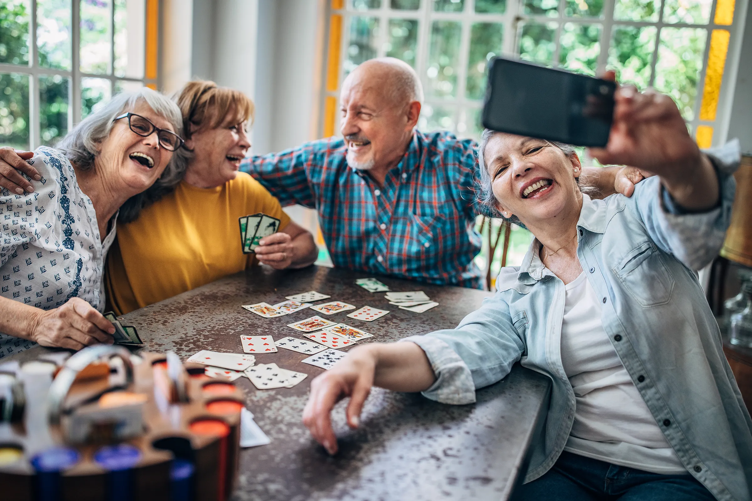 Four older friends taking selfie while playing cards